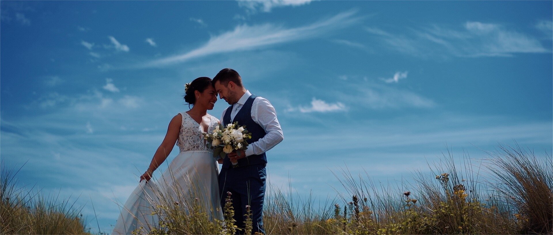Bride and groom on wedding day. Happy couple with flowers under blue sky.