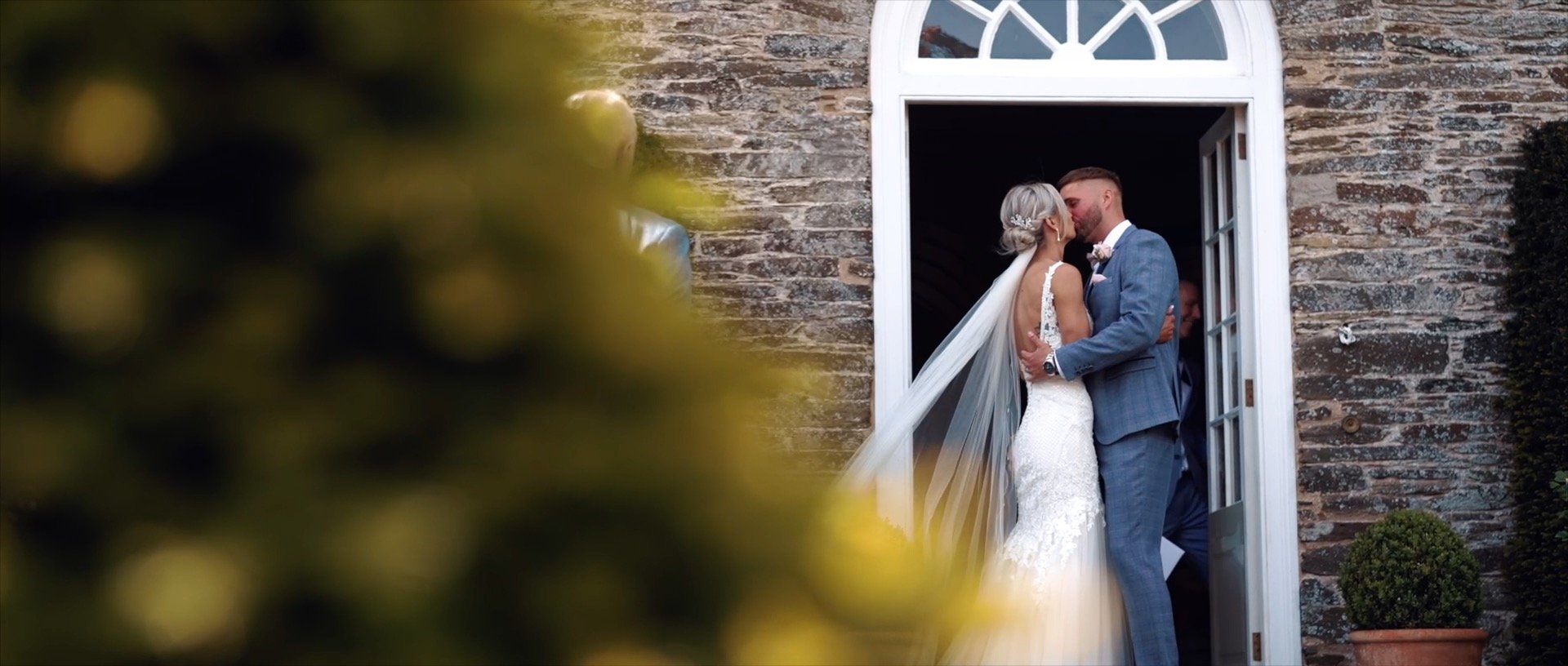 Newlyweds kissing at wedding venue. Bride in white dress, groom in blue suit. Romantic wedding photography.