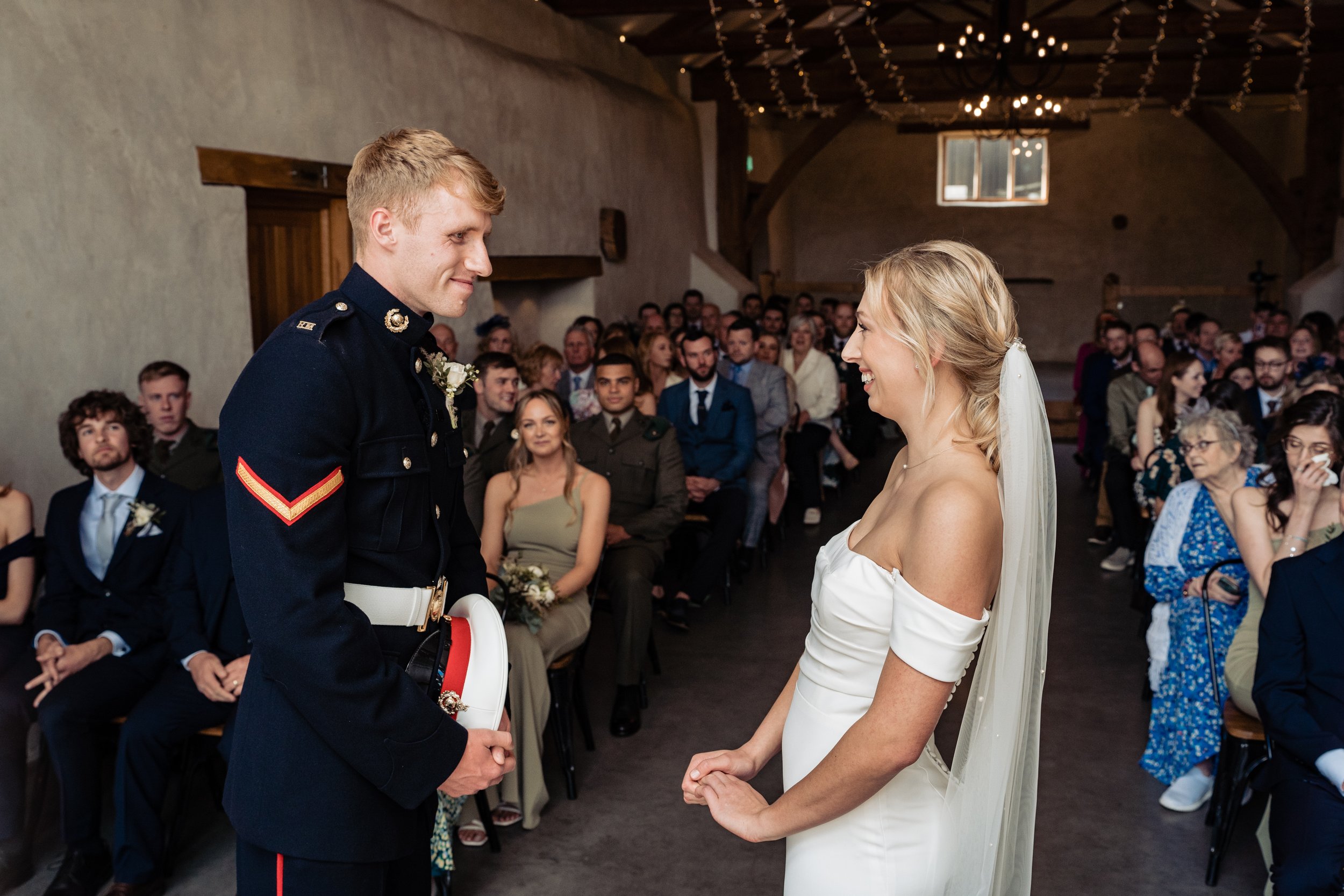 Bride and groom at wedding ceremony. Groom in military uniform. Wedding guests seated.