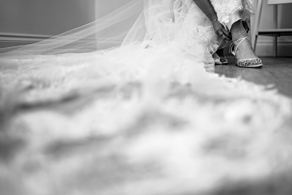 Devon wedding photography: Bride fastens her shoes. Wedding dress detail.