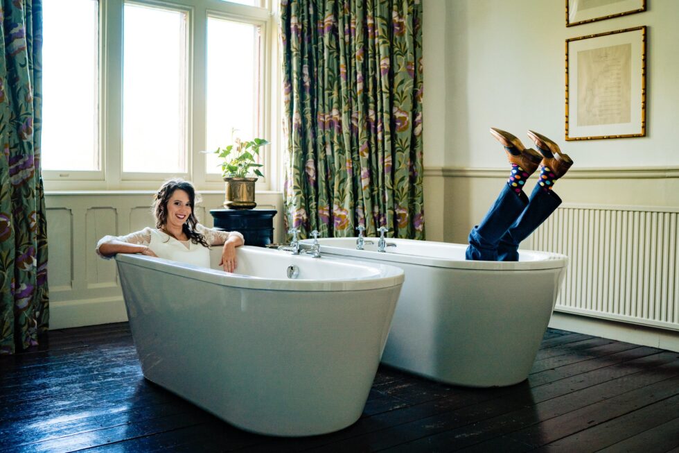Fun wedding photo: Bride relaxing in tub, groom's feet sticking out of another. Yeti Wedding Photography.