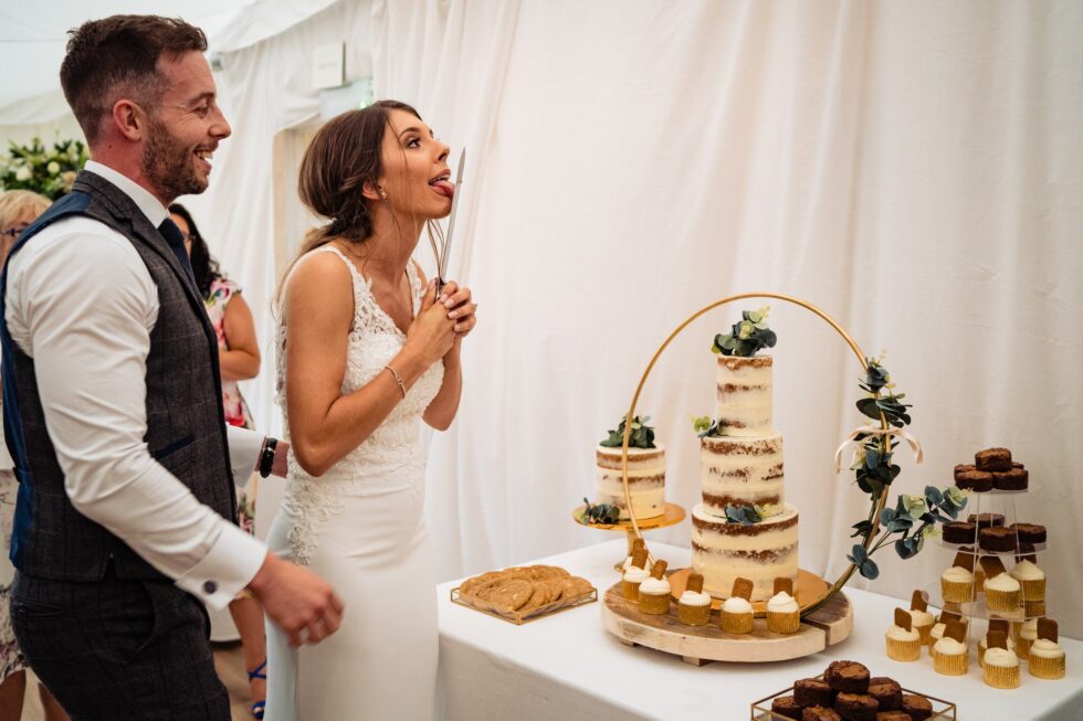 Devon wedding photography: Bride and groom with Biscoff cake and cupcakes. Funny moment with tongue out.