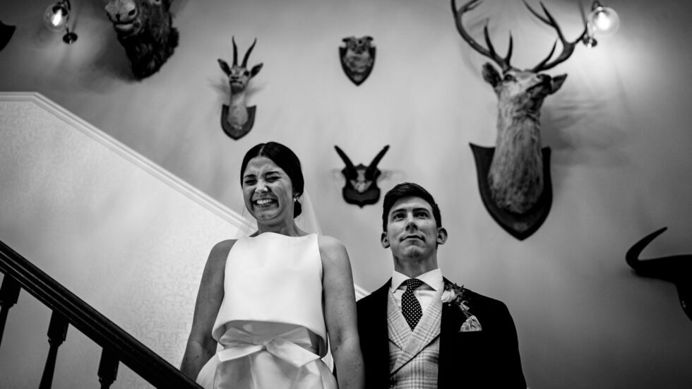 Funny Devon wedding photo. Bride and groom on stairs with animal head trophies. Yeti Wedding Photography.