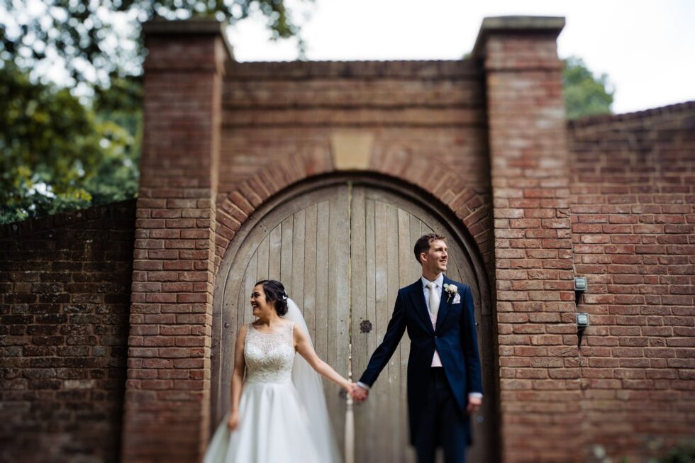 Devon wedding photography: Bride and groom hold hands in front of brick gate.