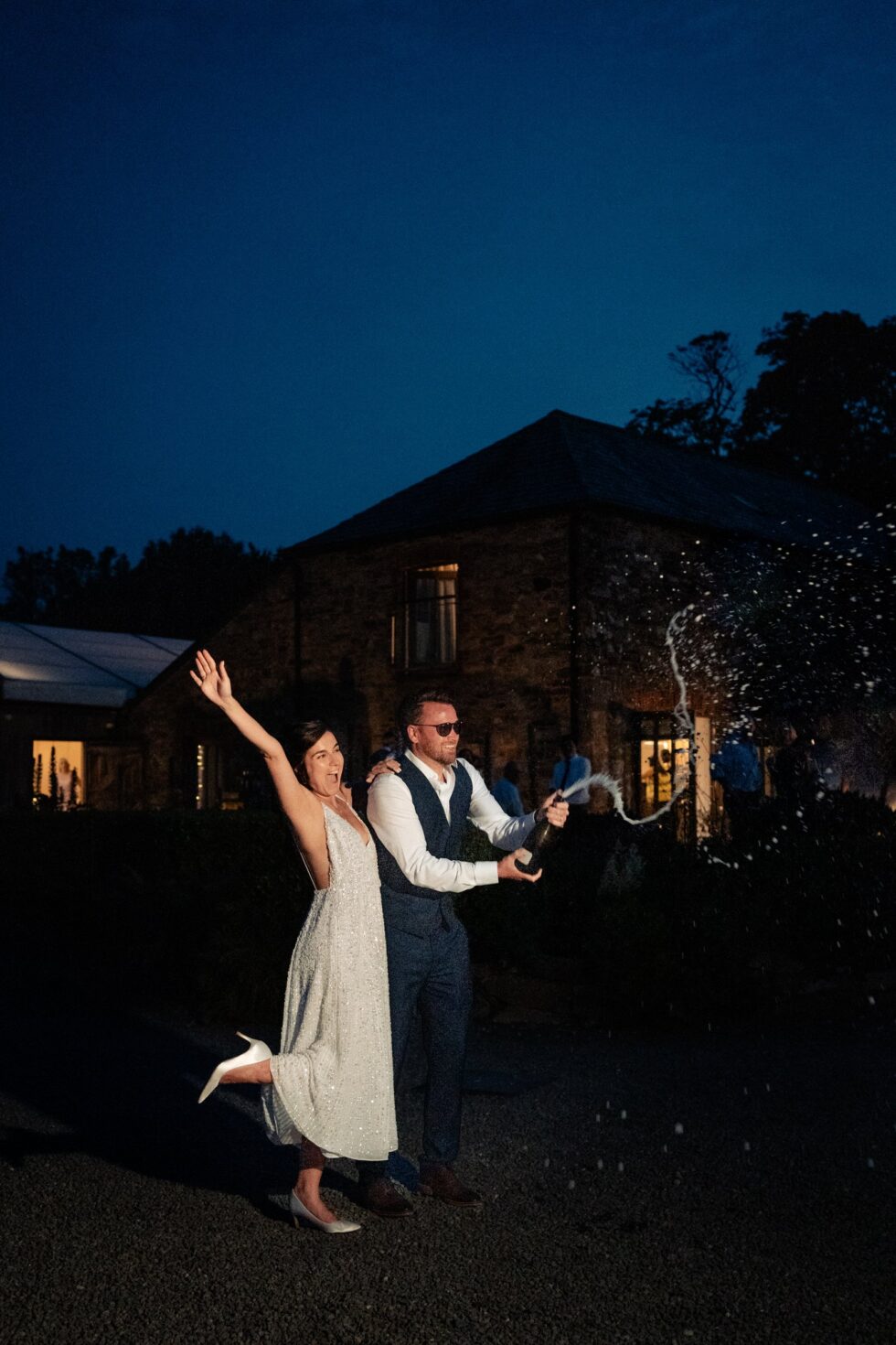 Cornwall wedding photography: Bride and groom pop champagne at Trevenna Barns, celebrating their special day.