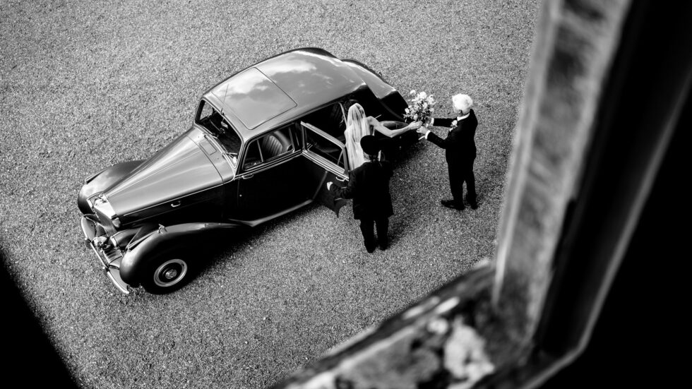 Bride getting flowers from dad at vintage wedding car. Yeti Wedding Photography.
