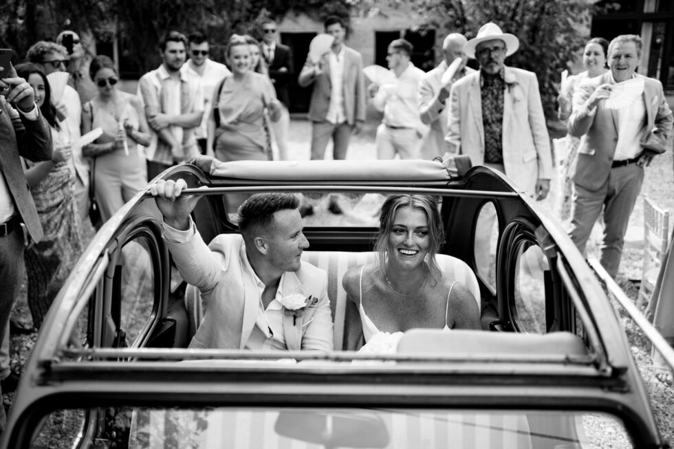 Manoir de Longeveau wedding photo. Bride and groom in Citroen 2CV, guests celebrating. Yeti Wedding Photography black and white.