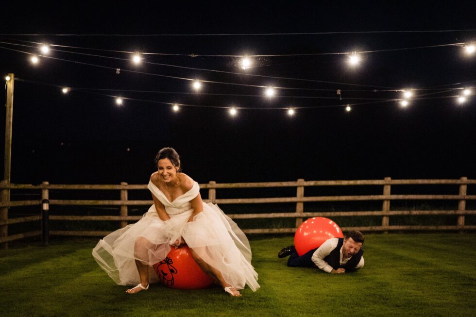 Devon wedding photography: Bride on space hopper, groom on ground laughing at Upton Barn wedding. Yeti Wedding Photography.