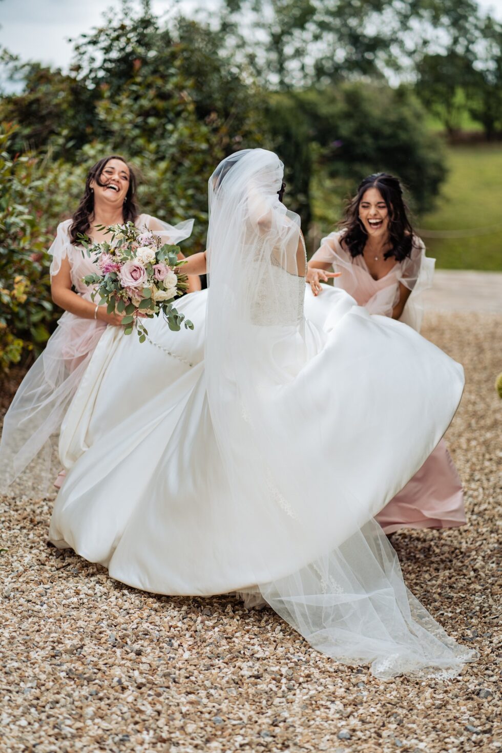Devon wedding photo: Bride twirling in gown, bridesmaids laughing. Veil blowing in wind. Yeti Wedding Photography.