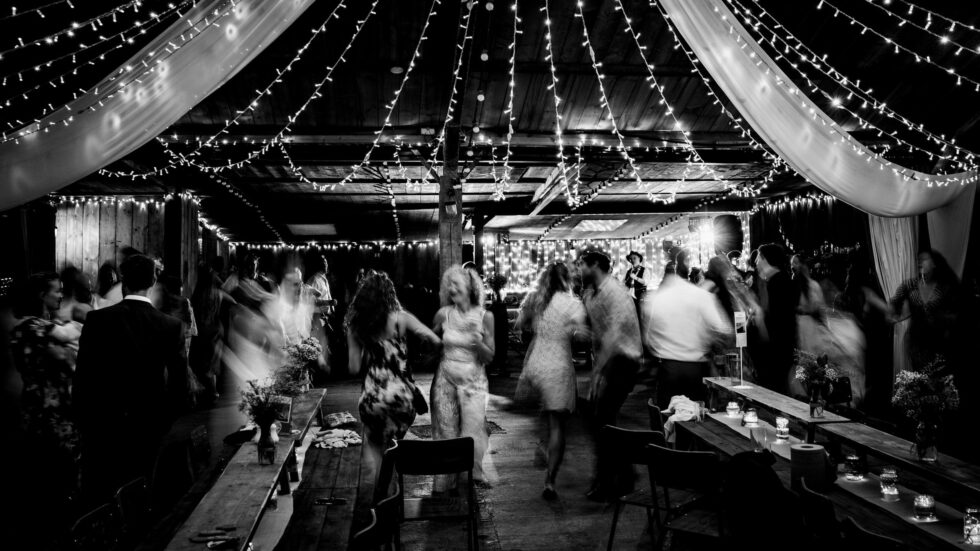 Black and white wedding photography: wedding guests dancing under string lights. Yeti Wedding Photography.
