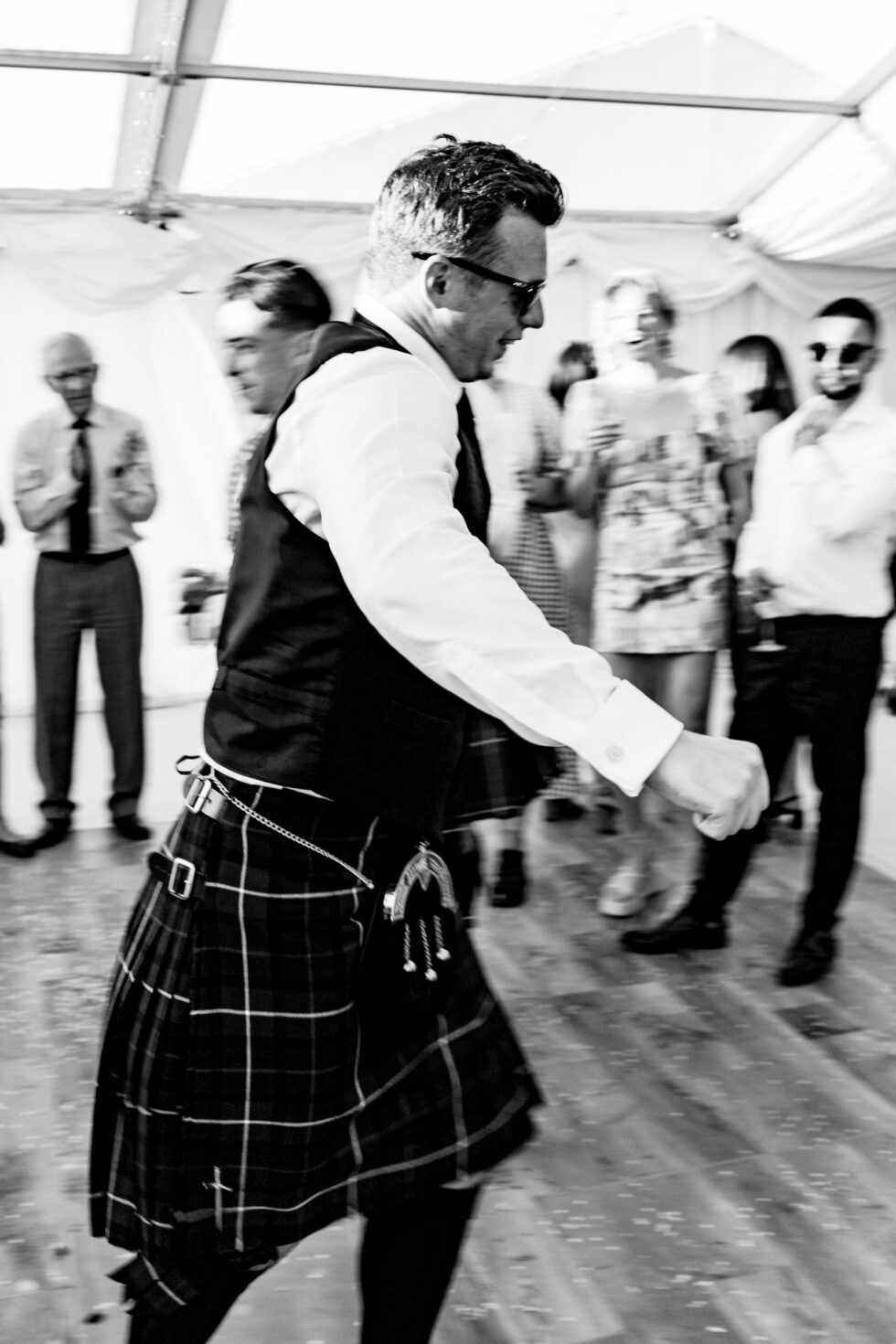 Groom dancing in kilt at Devon wedding. Fun, black and white wedding photography.
