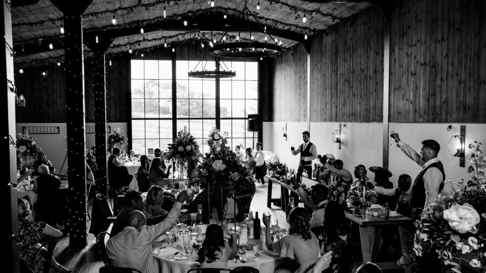 Black and white wedding photography of speeches at Upton Barn in Devon. Guests are raising their glasses.
