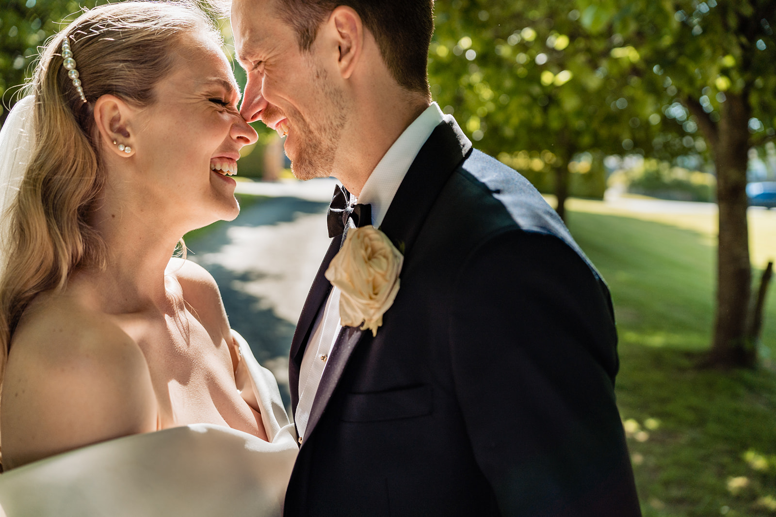 Bride and groom smiling at each other, with the bride wearing a strapless gown and a veil, and the groom in a tuxedo with a boutonnière.